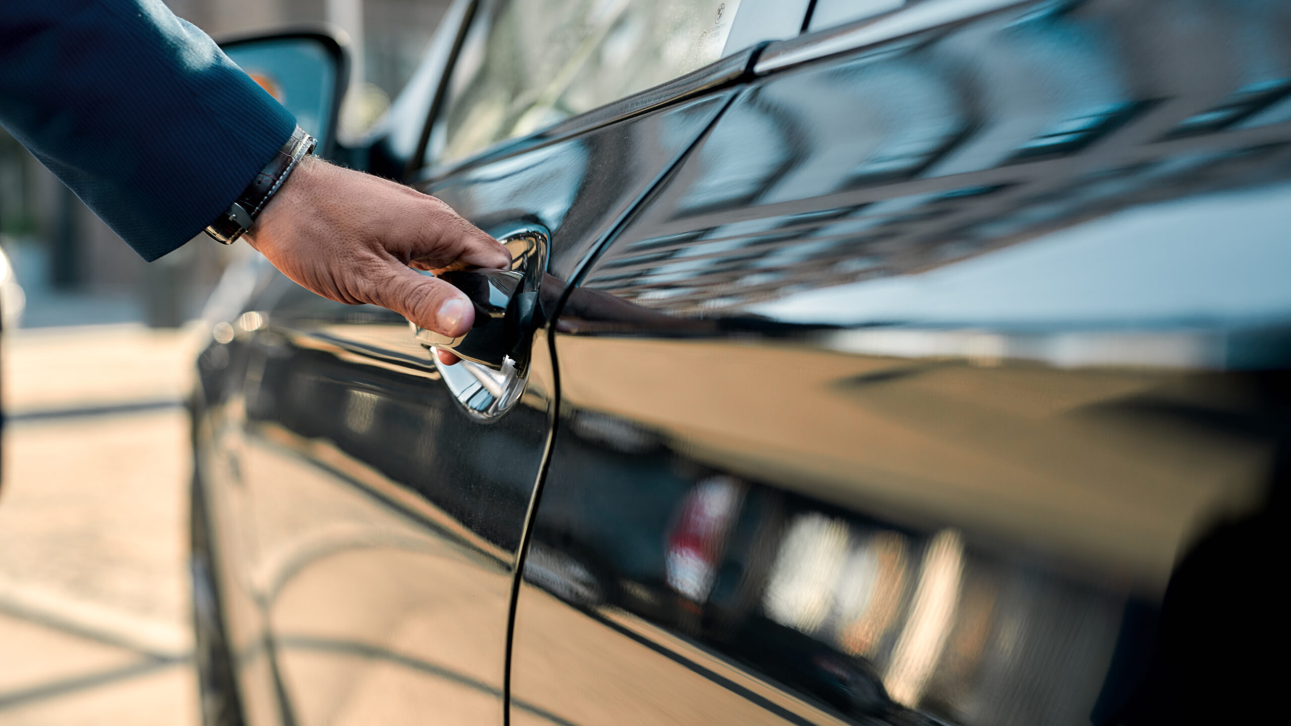 The hand of a traveller opening the door of a black car rental
